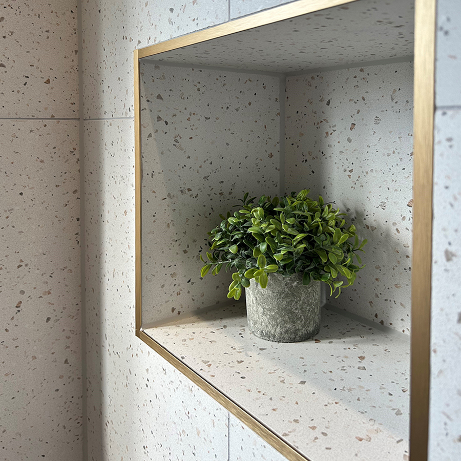 Terrazzo tiles in a shower with a gold tile trim edging an alcove shelf